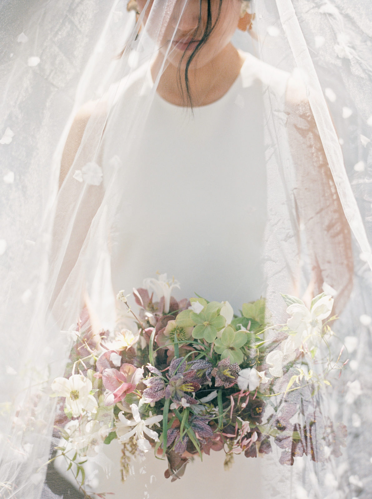 Bride wears floral applique veil over her face and bouquet while drenched in sunlight. Old world-inspired elopement.
