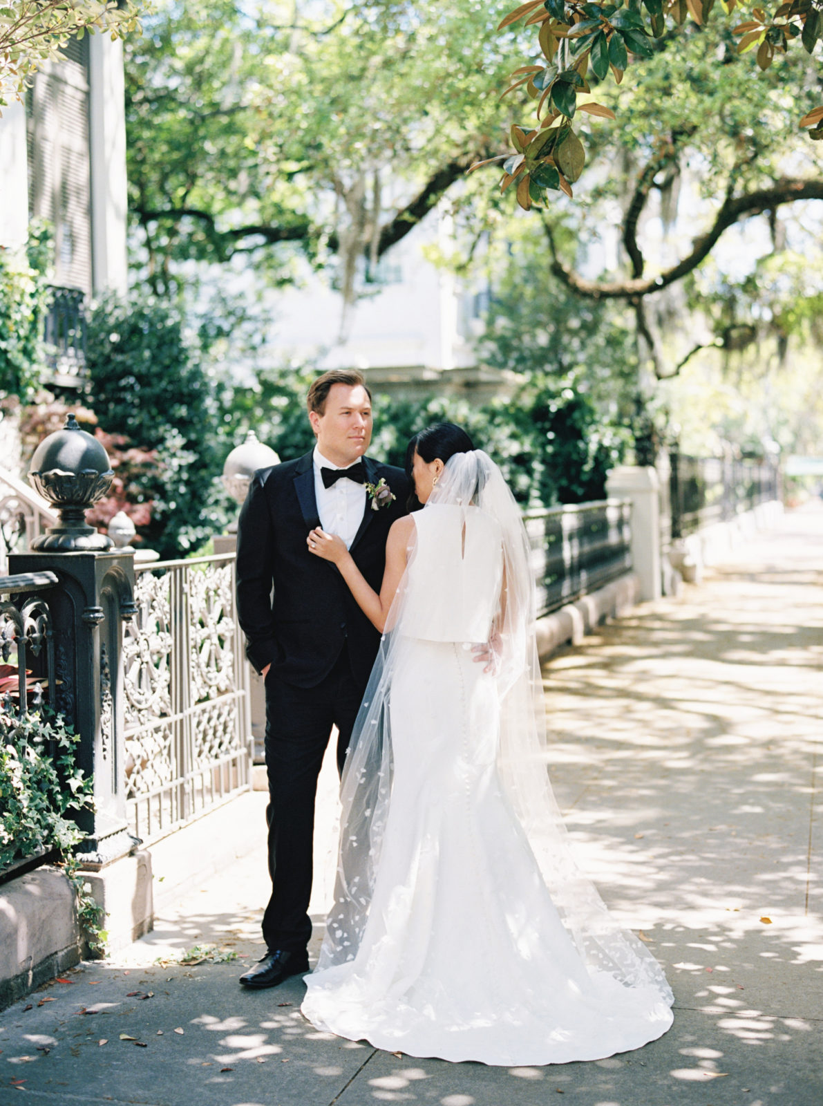 Groom holds bride's waist while bride nuzzles into groom on a sunny street in Savannah, Georgia. Old world-inspired elopement.