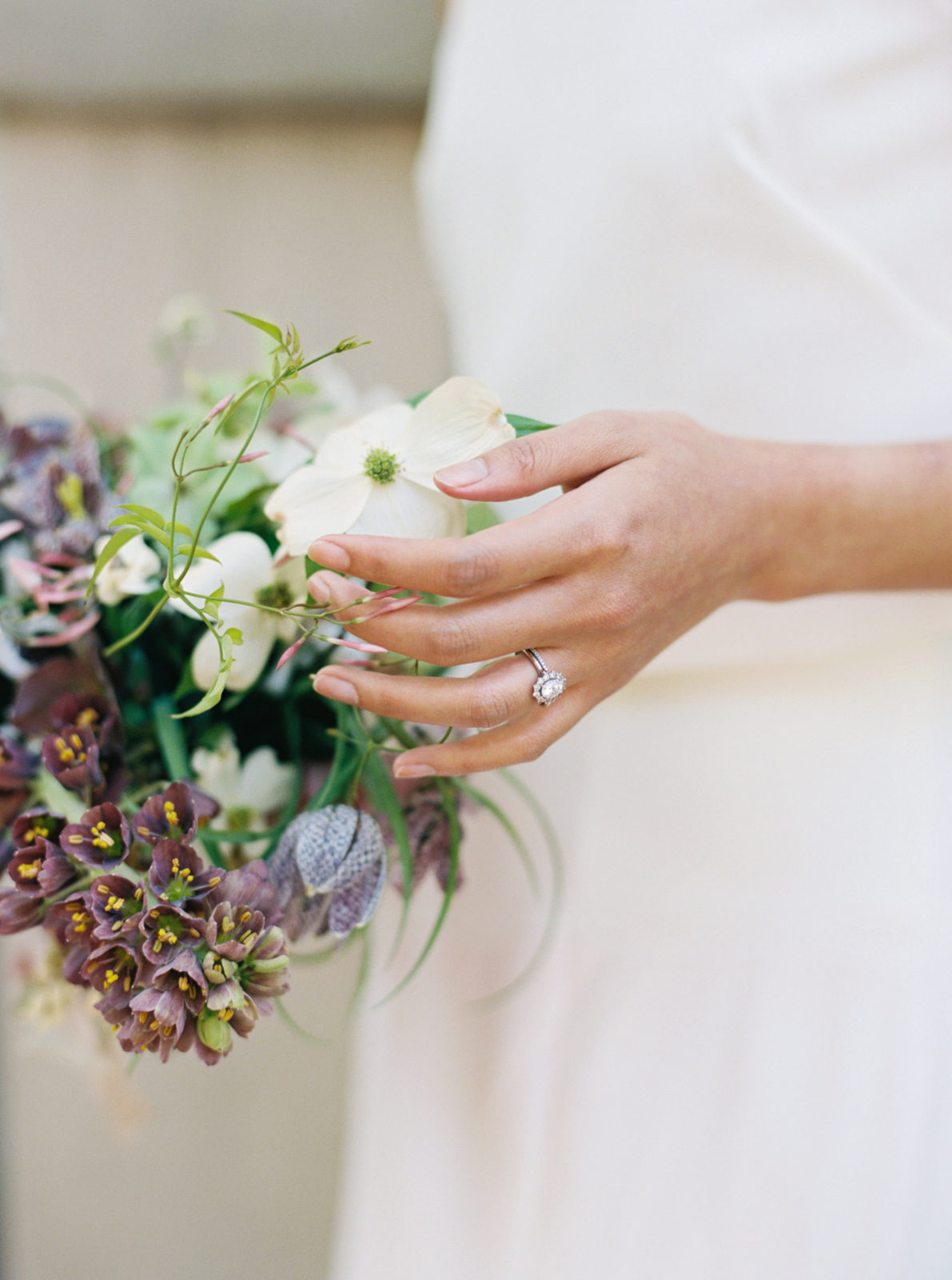 Bride gently holds a flower from her bouquet to show off her ring during her old world-inspired elopement.