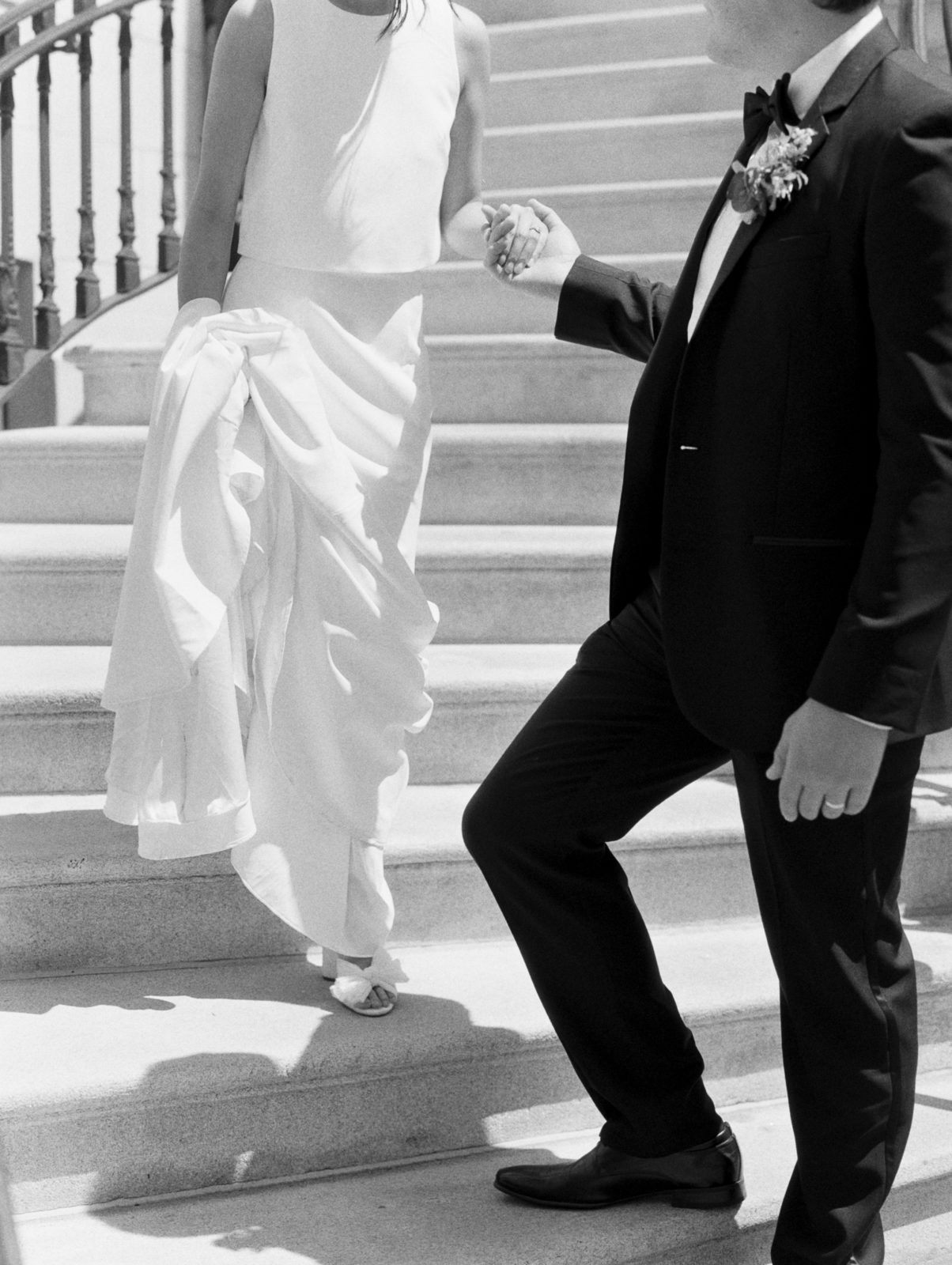 Groom helps bride down steps on black an white film.