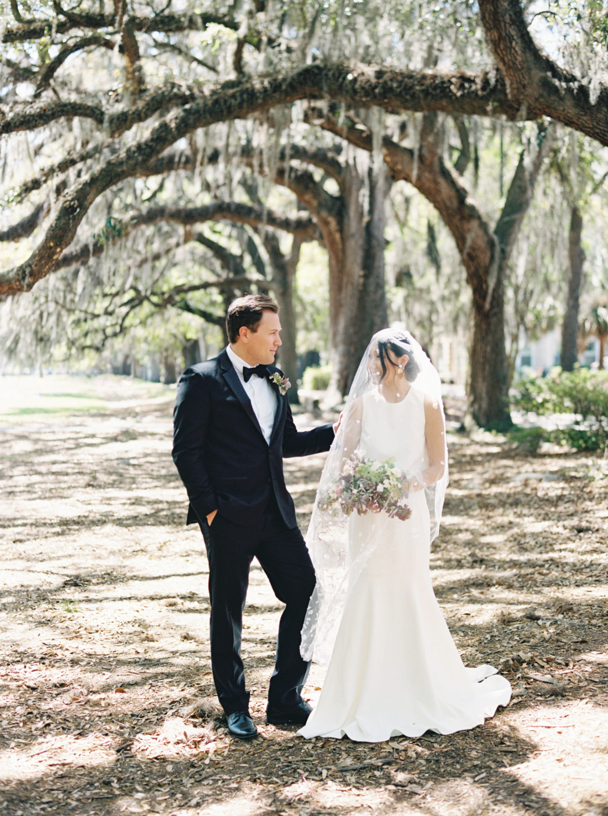 Bride and groom standing in a park covered in mossy trees in Savannah, Georgia. Old world-inspired elopement.