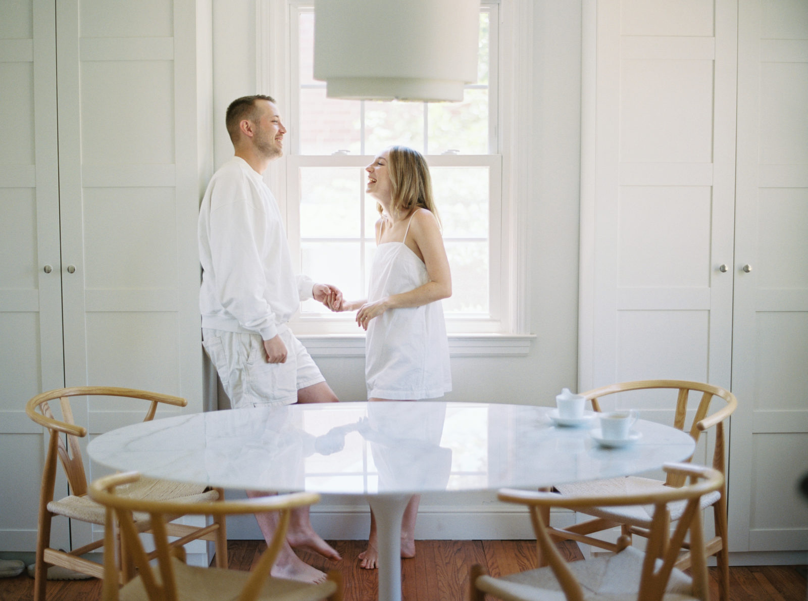 Couple laughing in the kitchen against a window.