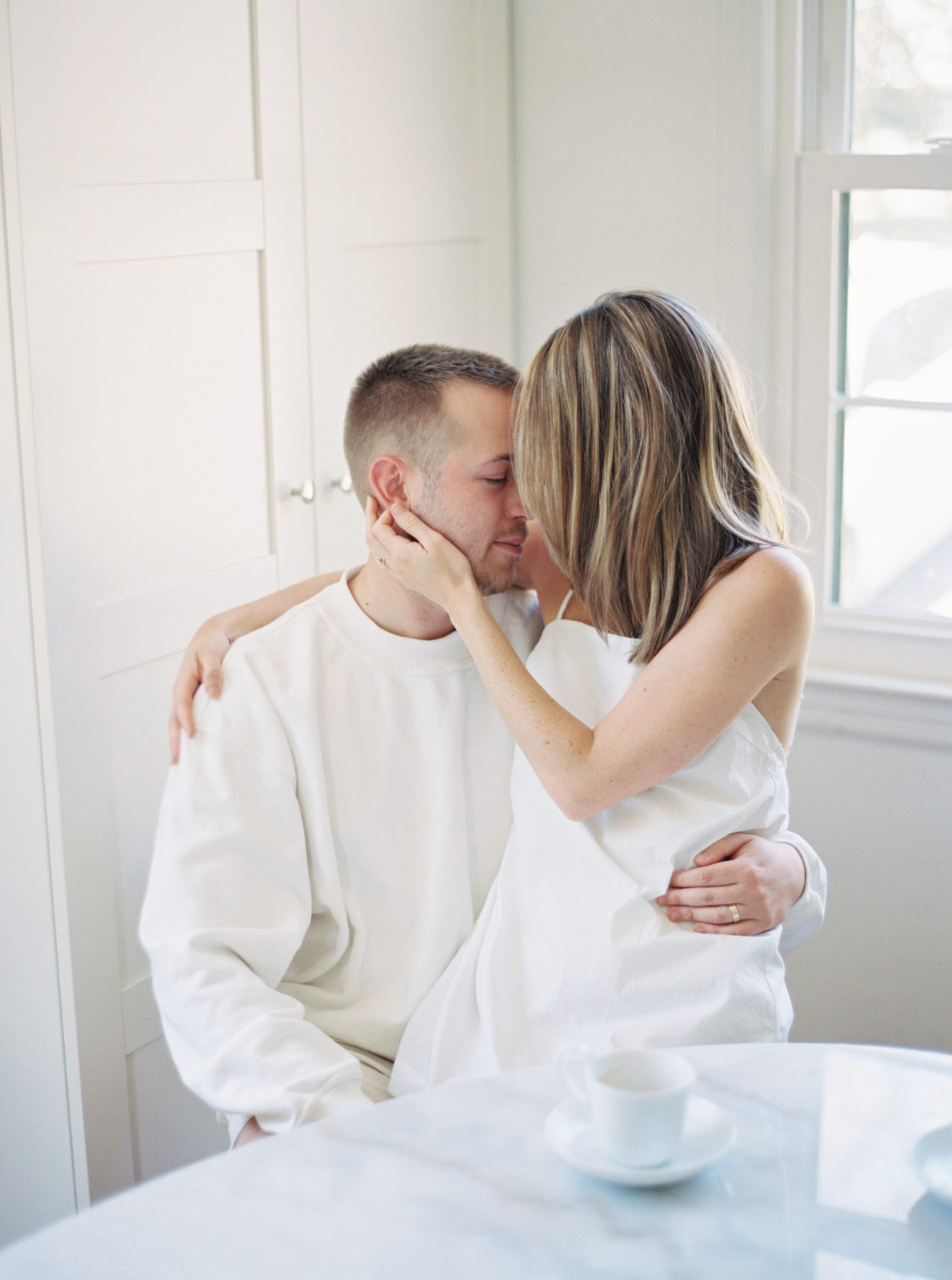 Lifestyle in-home session featuring minimal clothing and design. Couple at table snuggling.