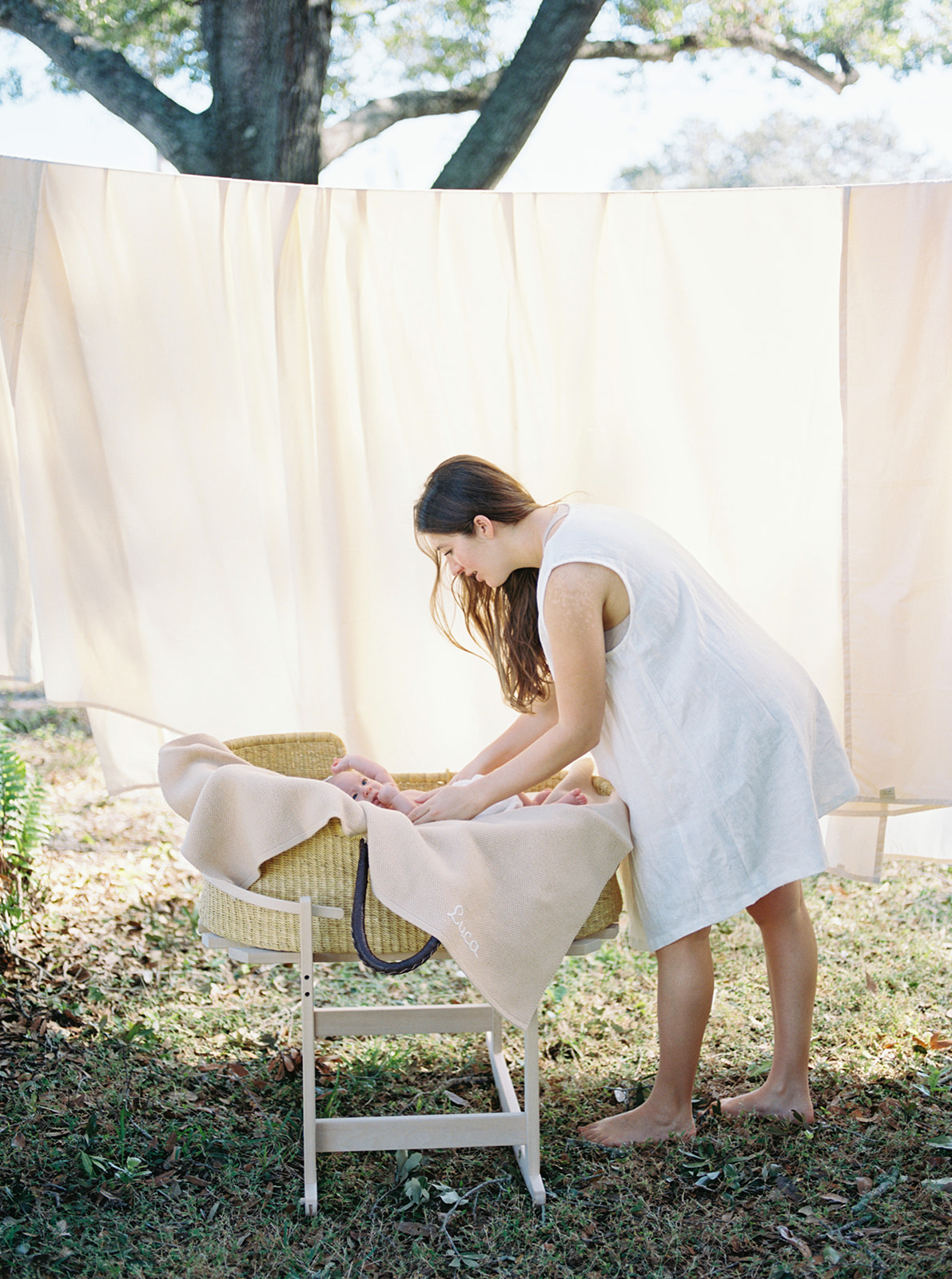 Mom dressed in short linen dress lifting baby out of organic woven moses basket during newborn portrait session.