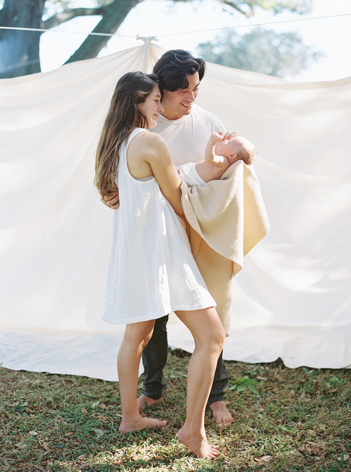 Mom and dad hold newborn baby in front of organic sheets in their garden.