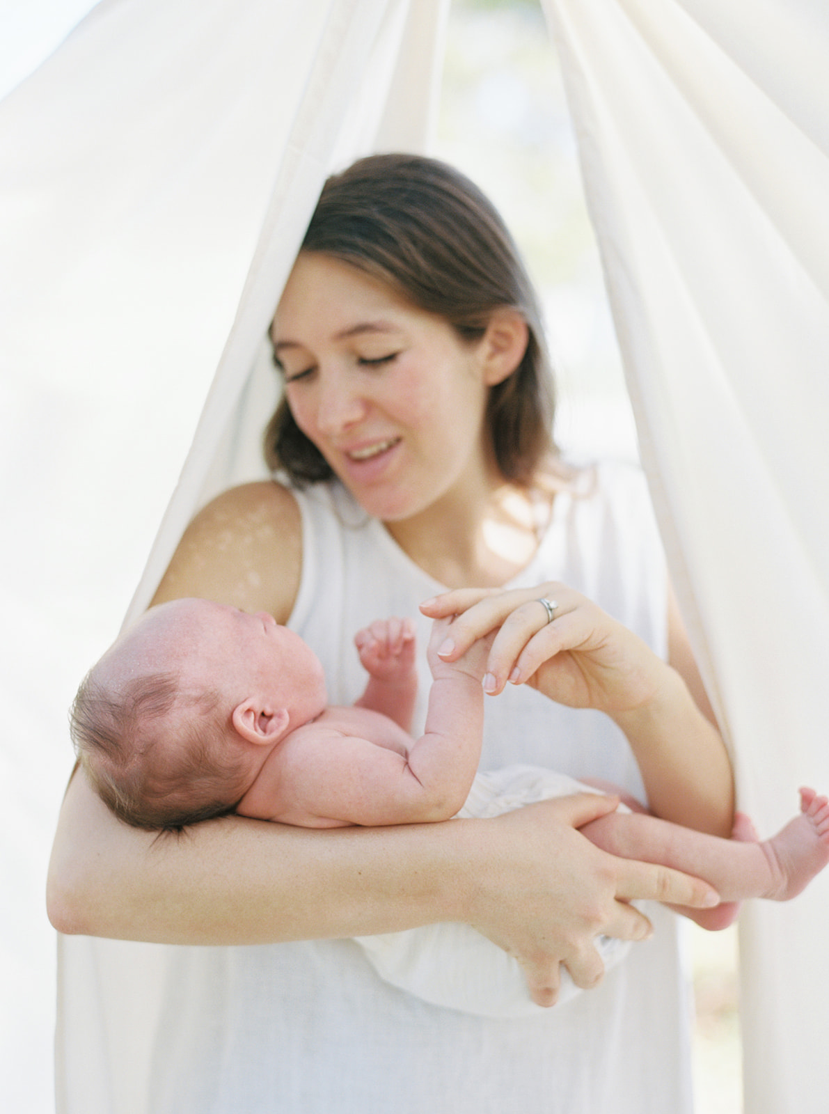 Mom holds baby's hand in front of organic sheets during newborn portraits.