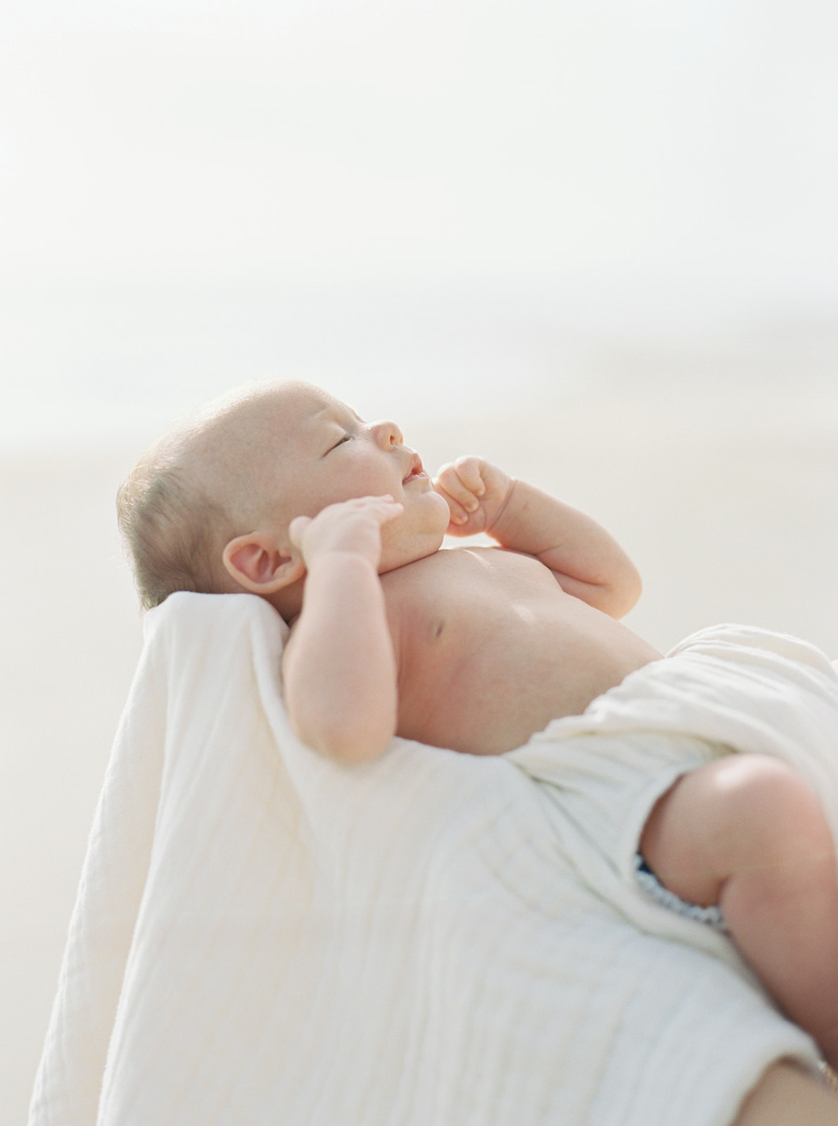 Baby is held in organic blanket during newborn beach portraits.
