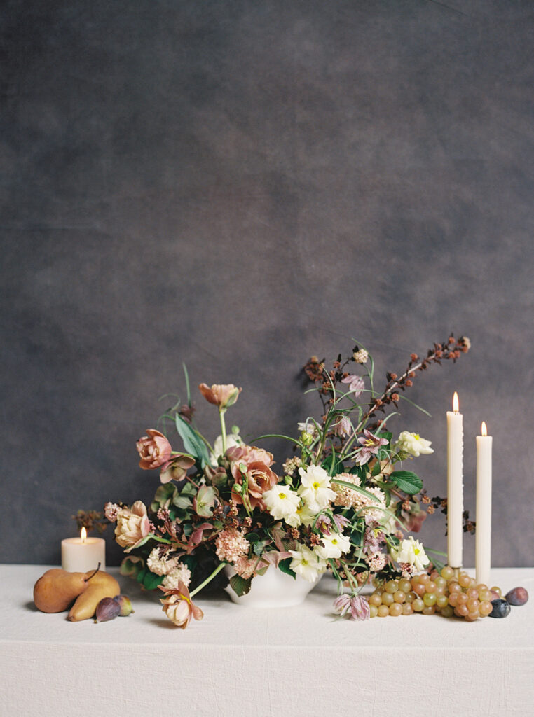 Branding image in a Nashville studio of a floral arrangement surrounded by candles and fruit against a dark backdrop