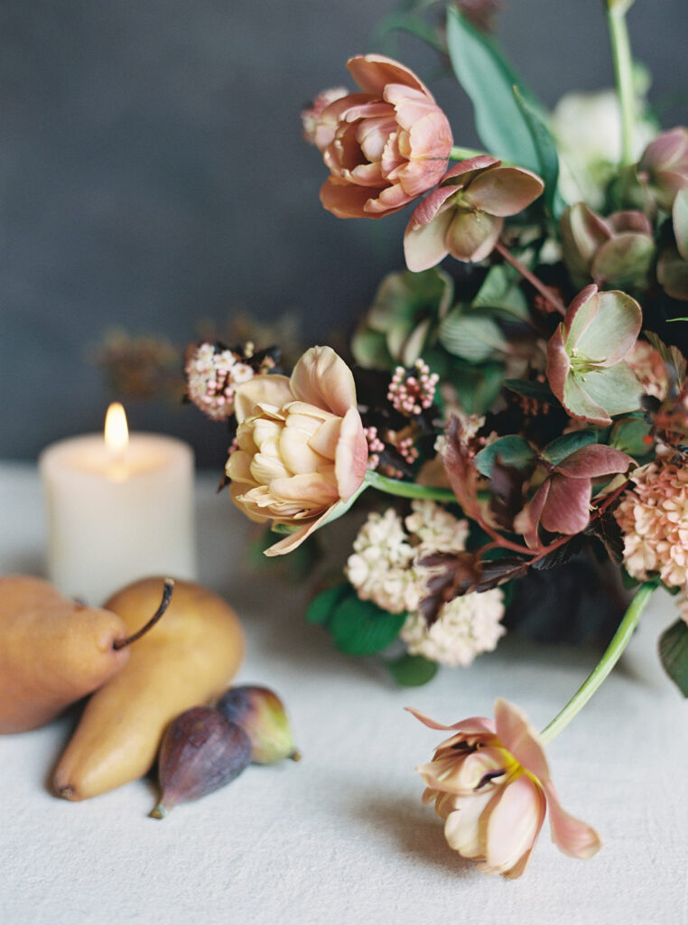 Moody flowers on a table next to a glowing candle