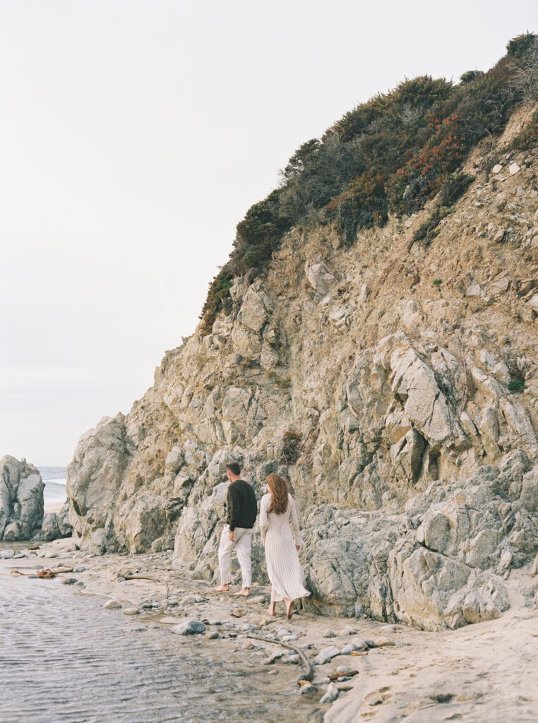 Couple walks along rocky coastline during their early maternity session in Big Sur