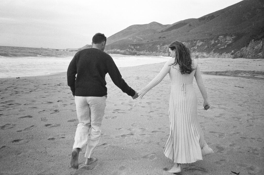 Couple hold hands and run down Gararapata Beach together for their early maternity session in Big Sur
