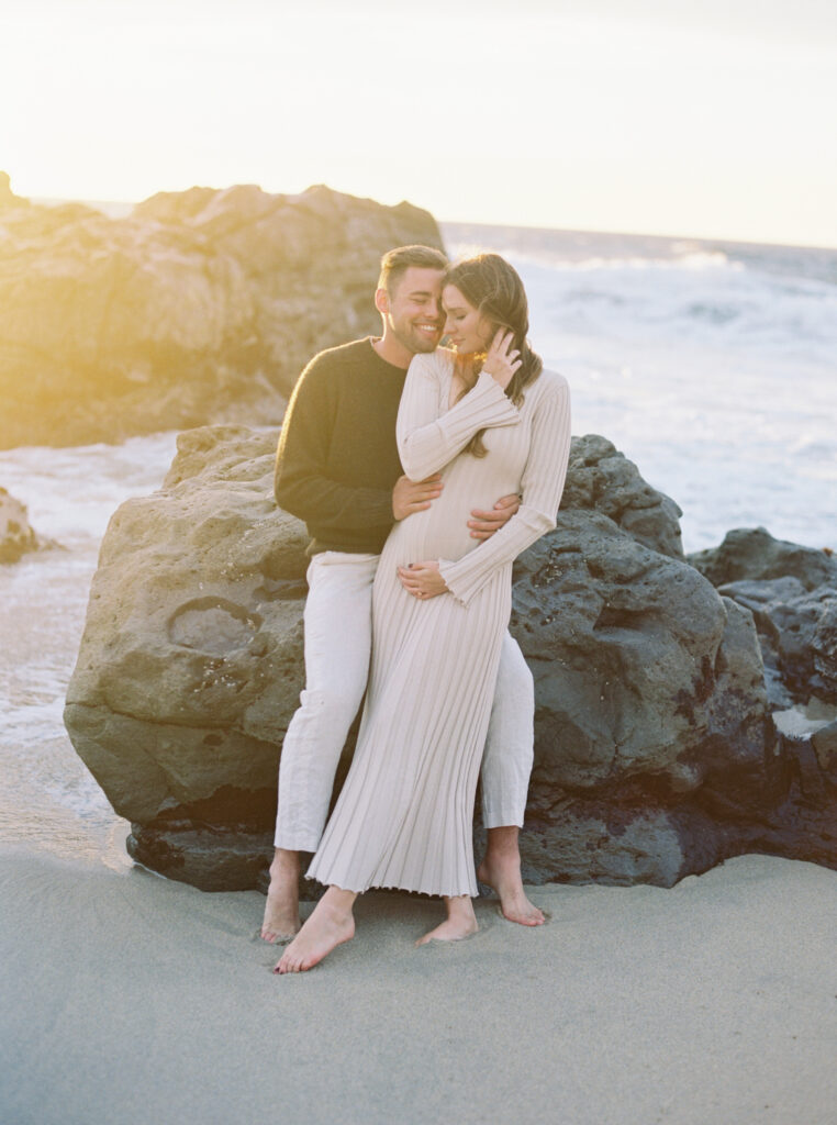 Couple nestled against rocks with the ocean in the background for their early maternity session in Big Sur