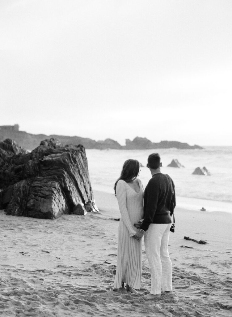 Couple looks out to the ocean during their early maternity session in Big Sur at sunset