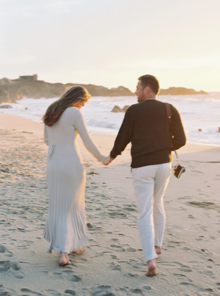 Couple holding hands and running down Garrapata Beach toward the sun for their early maternity session in Big Sur