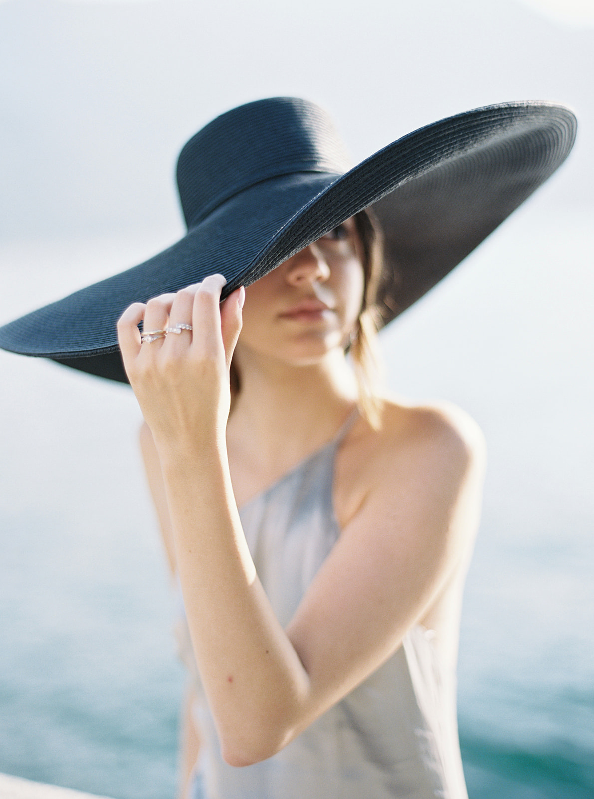 Girl in large black sun hat sitting on the shore of Lake Como, Italy for her portrait session