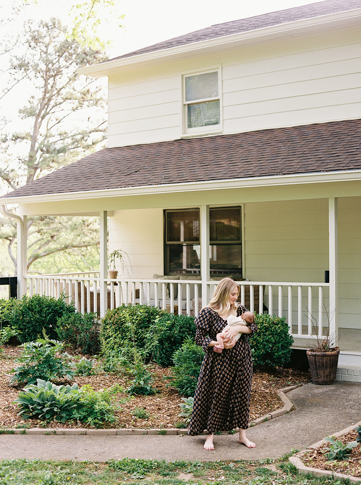 Mother holding baby outside house during in-home newborn family session