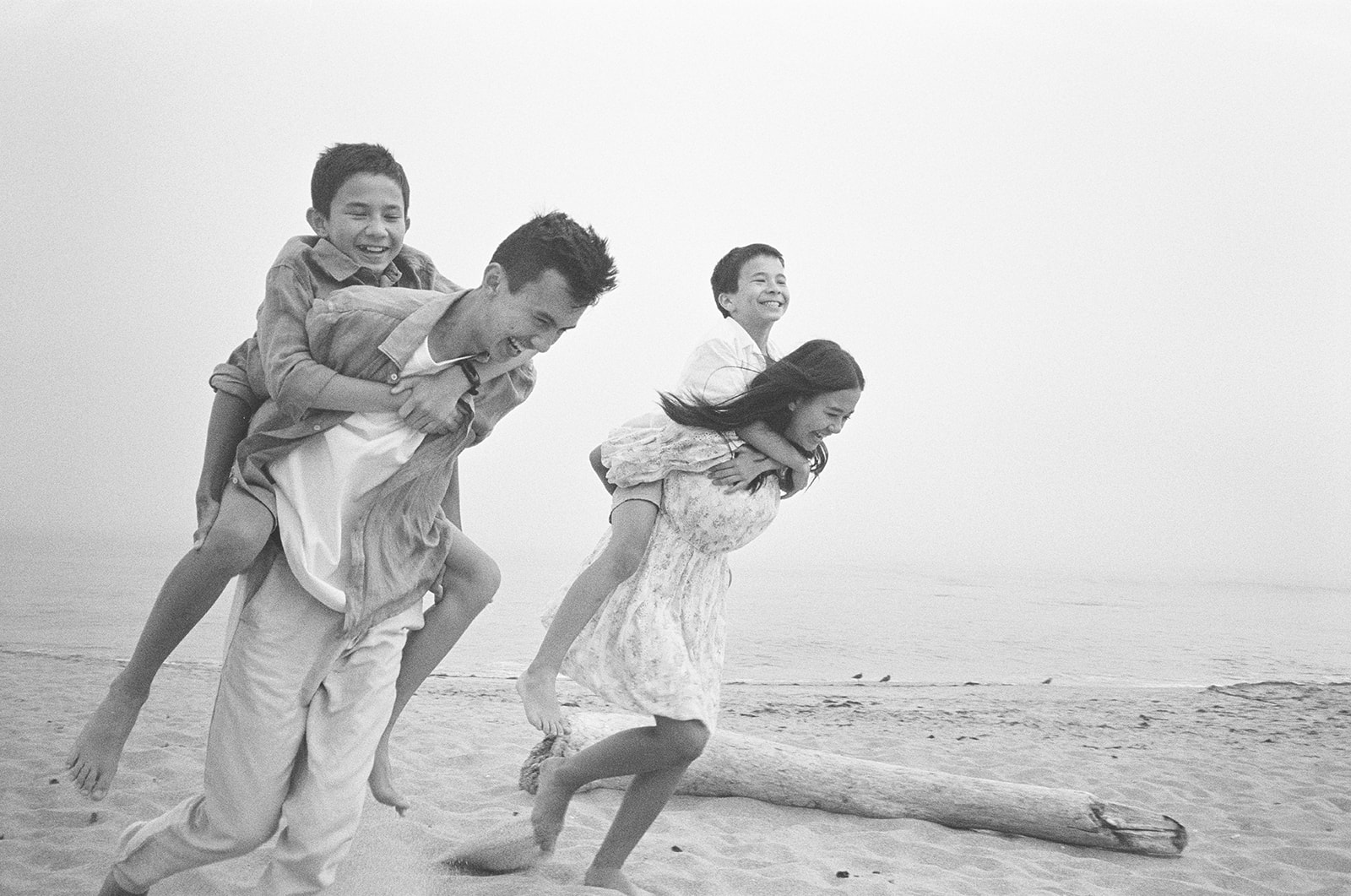 Four children race on piggy back photographed on black and white film on the beach in Northern California