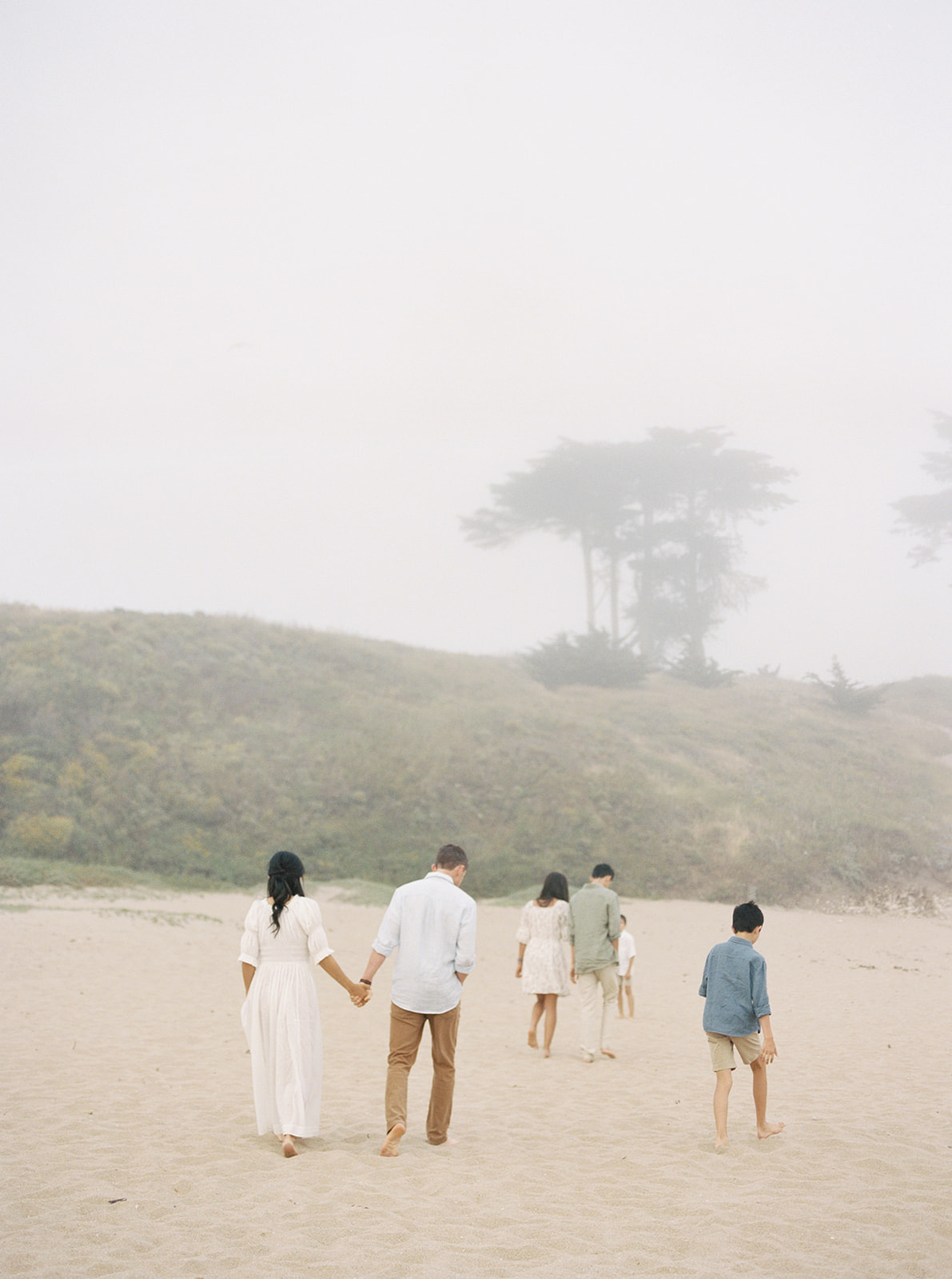 A husband and wife walk hand in hand down a Northern California beach during their family session