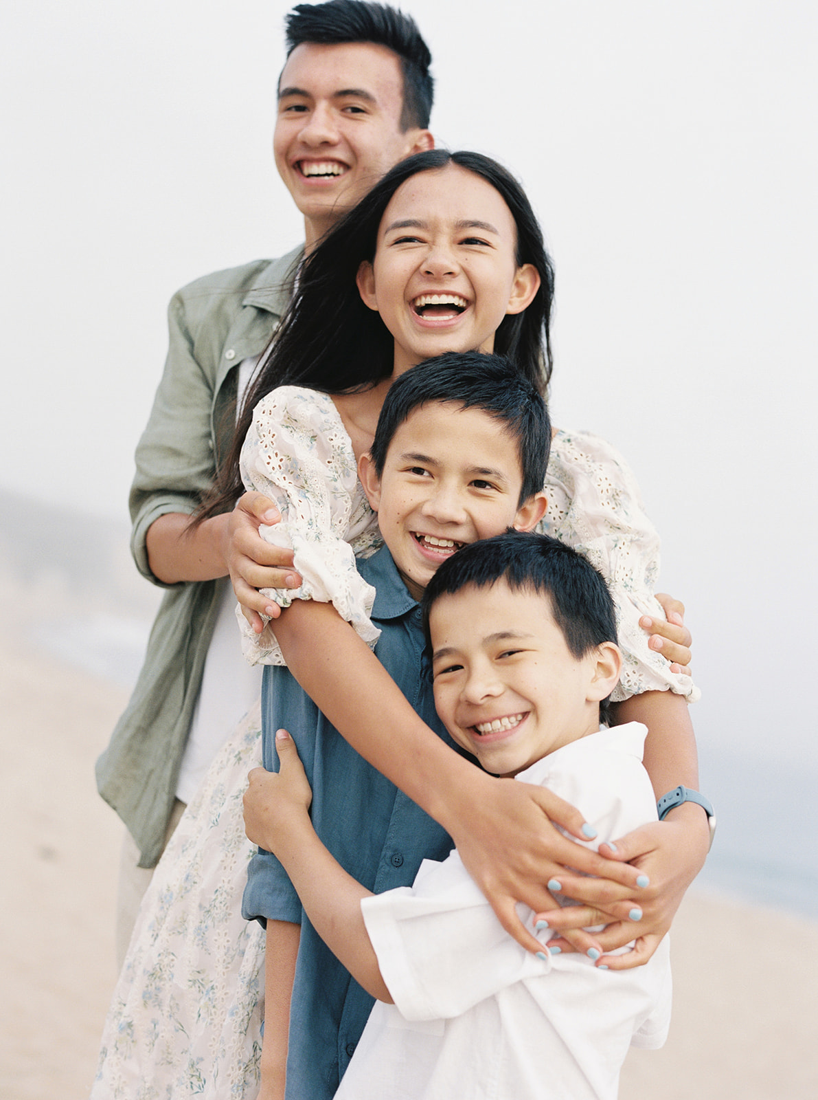 Siblings laugh while hugging on a Northern California beach while being photographed on film